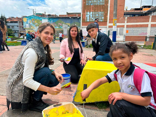 Una estudiante pinta junto a integrantes de la alianza durante la jornada de arte urbano en Bogotá